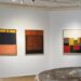 Drie abstracte schilderijen verlicht in een lichte galerieruimte