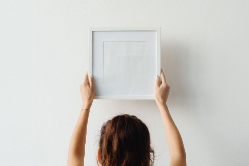 Persoon houdt een lege fotolijst tegen een witte muur bij het ophangen
