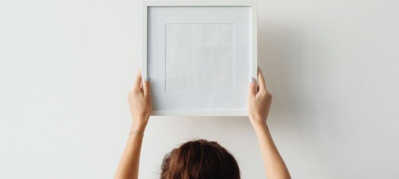 Persoon houdt een lege fotolijst tegen een witte muur bij het ophangen