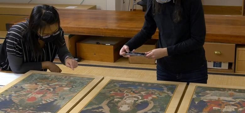 Twee medewerkers bekijken ingelijste kunstwerken voor conditiecontrole