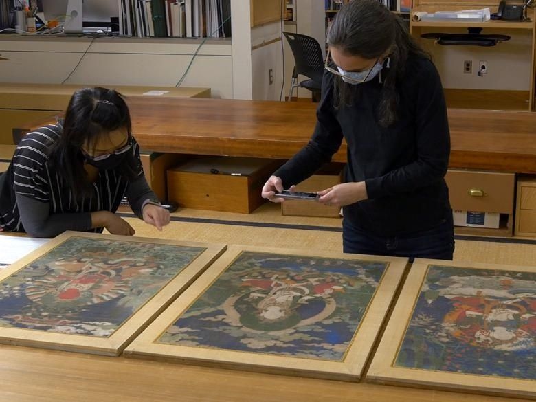 Twee medewerkers bekijken ingelijste kunstwerken voor conditiecontrole